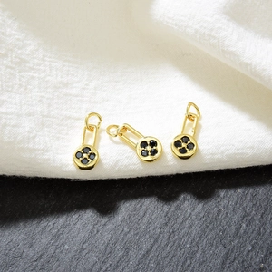 Three gold flower pendants with black zircons on a contrasting knit and stone background