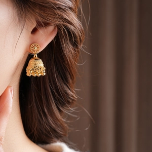 Close-up of golden vintage Jhumka earrings with intricate hollow patterns on a model