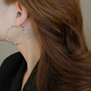 Detailed view of silver hoop earrings with twisted rope texture worn by a model