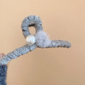 Detail von grauer Acryl-Haarklammer mit Stricktextur, weichem Pompon und Perlenakzent