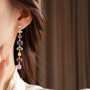 Detail showing elegant long drop earrings featuring multi-colored gemstones worn by a model