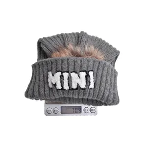 Berretto grigio in maglia con ricamo MINI e pompon in pelliccia pesato su bilancia digitale
