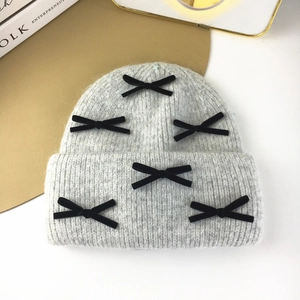 Detail view of a gray knit beanie with black ribbon bows on a minimalist background
