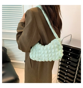 Detail of mint green popcorn fabric shoulder bag worn by model over a brown coat