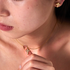 Close-up of a model wearing a gold-plated cross necklace and matching zircon earrings
