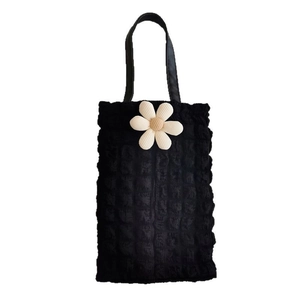 Close-up of black bubble textured tote bag with a white daisy floral accessory