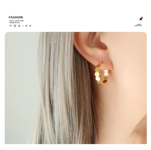 Close-up of golden hoop earrings with textured sequin link design worn by a model