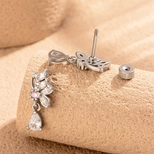 Silver butterfly cartilage earrings with pink and white zircon stones on beige texture