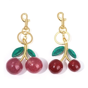 Detail of red cherry keychains in two sizes with gold glitter resin and green leaves