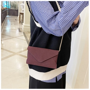 Detail showing a burgundy envelope crossbody bag with a gold chain strap on a model