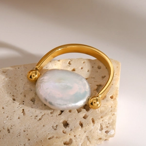 Détail d'un bracelet jonc doré avec une perle baroque sur un support en pierre beige