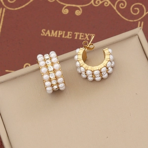 Macro detail of gold C-shape stud earrings featuring rows of pearls and clear zircon stones