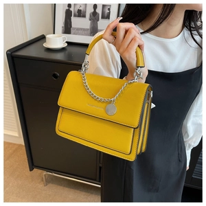 Detail of yellow leather handbag showing silver chain decor and textured flap surface
