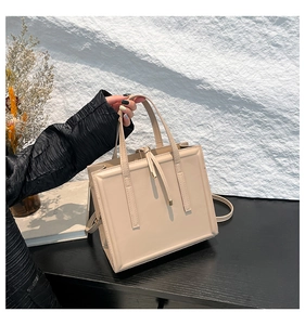 Elegante borsa tote in pelle beige su tavolo in legno scuro con accessori decorativi