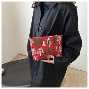 Détail d'une pochette festive en tissu rouge avec motif sapins tenue par un mannequin