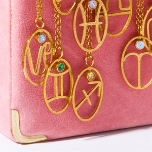 Detailed view of six gold zodiac necklaces with varied gemstones on pink velvet background