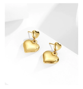 Detailed close-up of golden double heart earrings on a minimalist white paper background