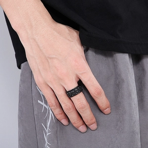 Detailed close-up of a men's matte black stainless steel ring with carved skull patterns