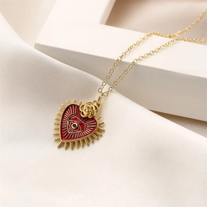 Gold heart necklace with red enamel eye pendant and rose detail on white fabric