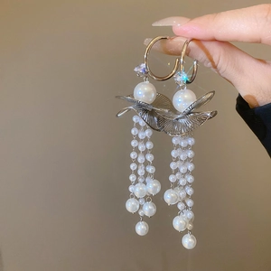 Close-up of golden tassel earrings with white pearls and ruffled leaf metal detail