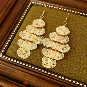 Detailed close-up of golden leaf-shaped tassel earrings on green velvet stand