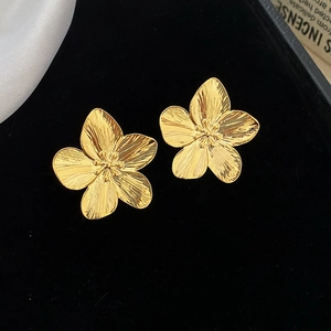 Dettaglio di orecchini a fiore dorati vintage con finitura in metallo spazzolato su velluto