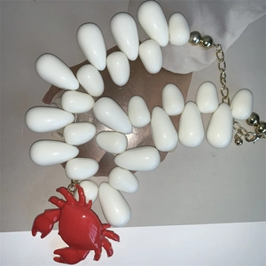 Detailed close-up of white teardrop beads necklace with red crab pendant and golden clasp
