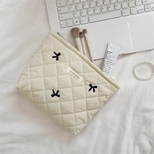 Detail of cream quilted makeup bag with bow embroidery on white bedding background