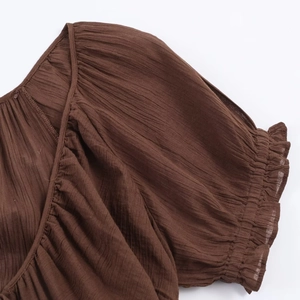 Close-up of brown pleated dress fabric with ruffled cuffs and smocked neckline details