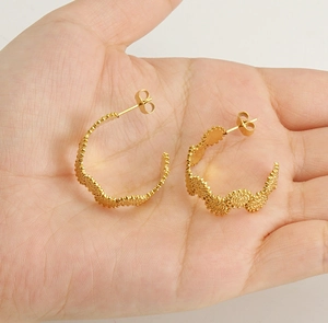 Détail de boucles d'oreilles fleurs dorées à texture ondulée tenues en main