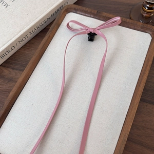 Detail of pink faux leather bow hair clip with long ribbons on a decorative wooden tray