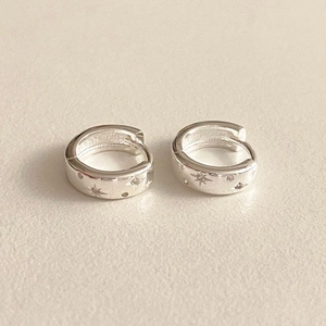 Macro shot of silver hoop earrings featuring engraved star patterns and cubic zirconia stones