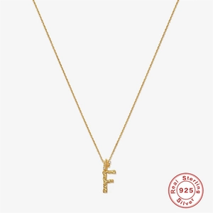 Macro shot of 925 sterling silver letter F pendant with irregular textured gold finish