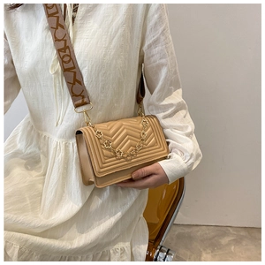 Detail of beige quilted crossbody bag featuring a golden clover chain and jacquard strap
