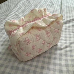 Detail der beige gesteppten Kosmetiktasche mit rosa Schleifenmuster auf Karo-Stoff
