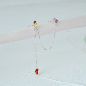 Macro detail of S925 silver tassel earrings with colorful zirconia gems on a white bar