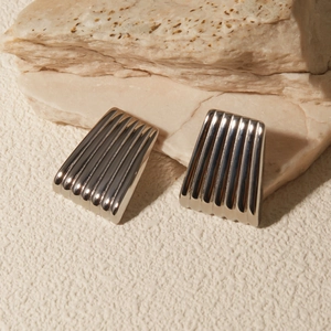 Macro view of trapezoid metal earrings with vertical textured stripes on natural rock