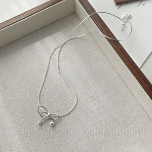Detail shot of a silver bow pendant necklace on a textured fabric jewelry tray