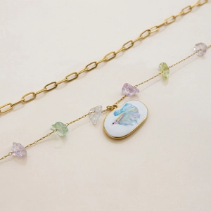 Macro view of gold-toned layered necklaces with colorful stones and hand-painted fish pendant