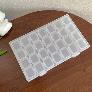 Clear plastic 28-grid jewelry organizer box with flip lid on a dark wooden surface