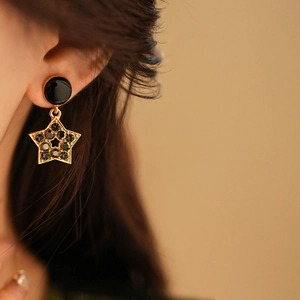 Gros plan de boucles d'oreilles étoile dorées avec strass noirs portées par un mannequin