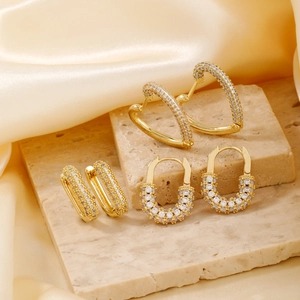 Dettaglio di tre orecchini placcati oro con zirconi pavé e forme geometriche eleganti