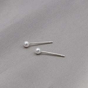 Macro shot of minimalist round white pearl earrings with S925 silver studs on grey fabric