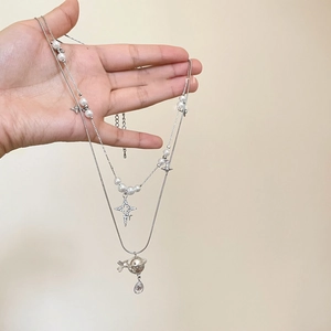 Close-up of double-layer necklace with pearl stars and Saturn pendant on a hand