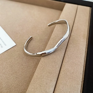 Detailed close-up of a silver wavy open bangle on a warm textured jewelry display
