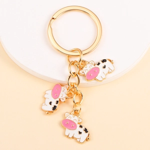 Detailed view of golden keychain with three cute enamel cow pendants on white base
