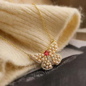 Elegant gold butterfly pendant necklace featuring pearls and a red gemstone on knit fabric
