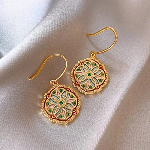 Close-up of enamel flower earrings with green gemstones and gold finish on silk