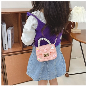 Pink girl's jelly crossbody bag with pearl handle and charms shown on a child model