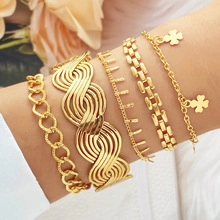 Detail of five-piece gold-tone bracelet set with clover charms on a woman wrist